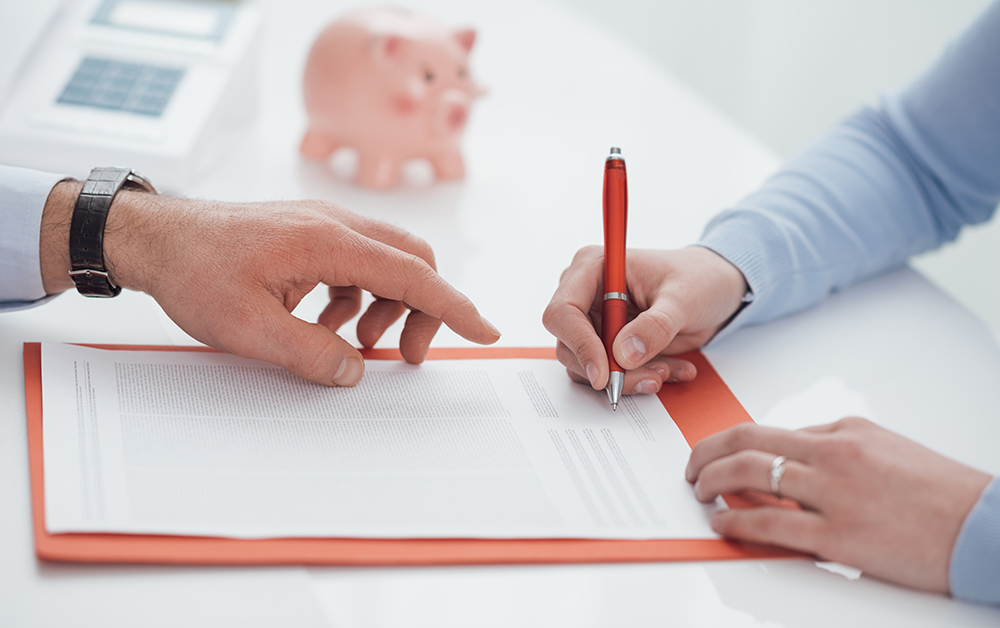Woman signing a contract and financial advisor pointing at the document, financial planning and banking concept